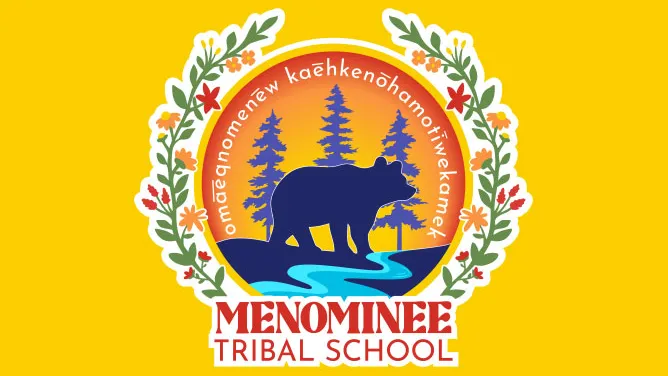 Logo for Menominee Tribal School featuring a bear silhouette standing by a river with pine trees in the background, surrounded by a circular border with floral decorations. The text “Menominee Tribal School” appears below, and Menominee language text is written around the top of the circle.